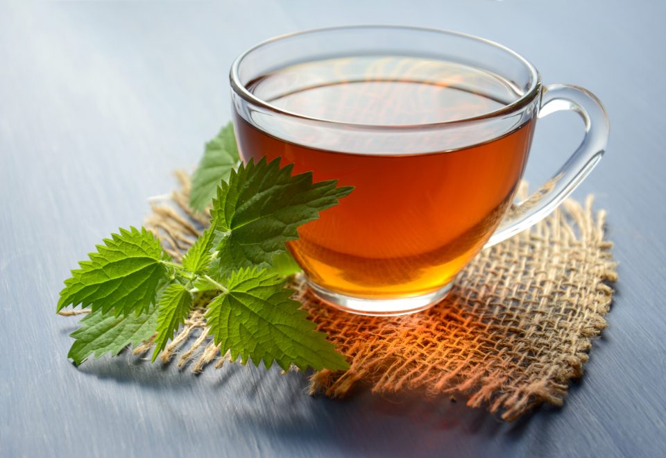 A glass cup of herbal tea with loose herbs beside it