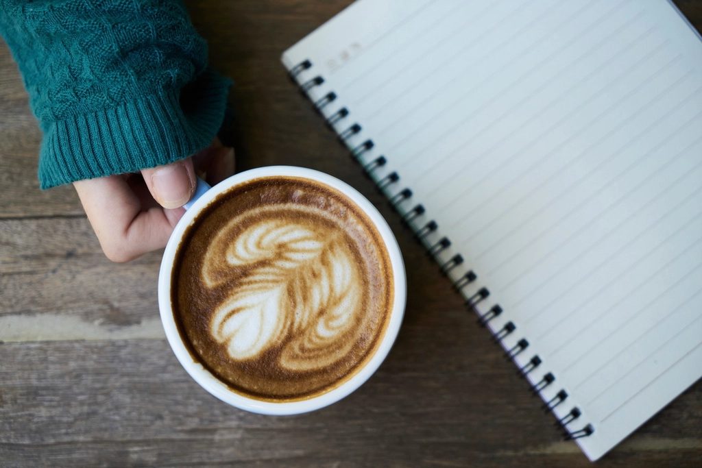 A latte served in a glass, held in two hands